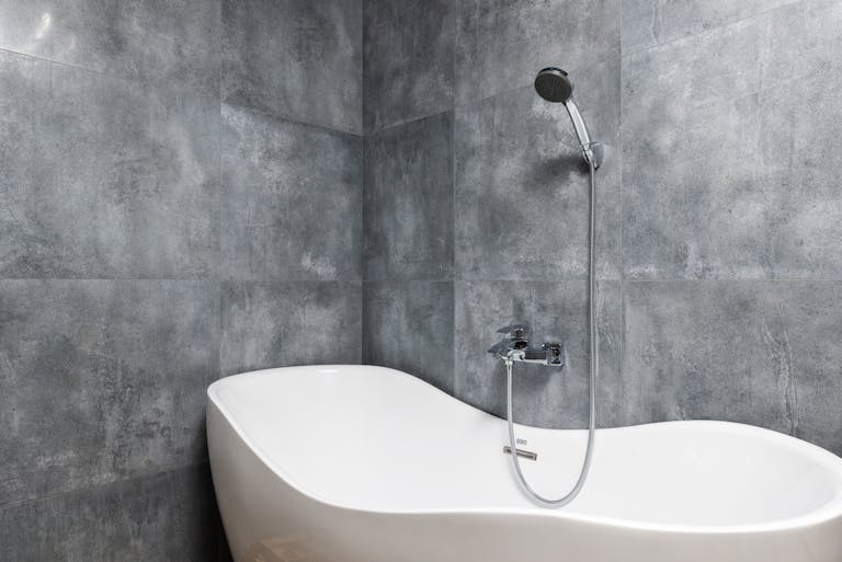 Bathroom interior with bathtub under shower on tile wall